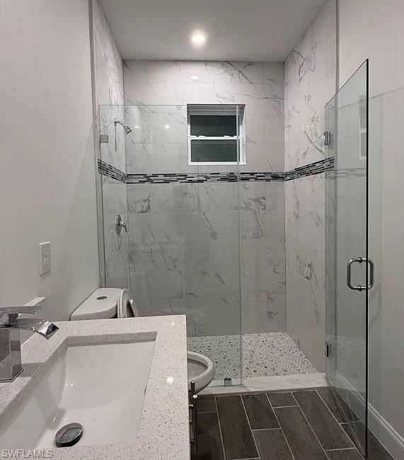 Bathroom featuring vanity, a marble finish shower, and wood tiled floors