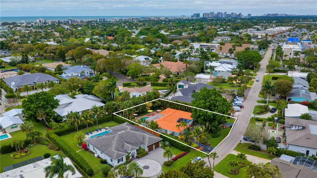 Aerial view of residential area with property parcel outlined, city skyline, and a nearby body of water