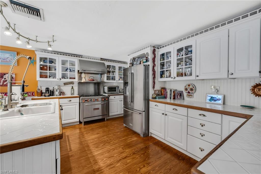 Kitchen featuring tile countertops, premium appliances, white cabinets, and glass fronted cabinets