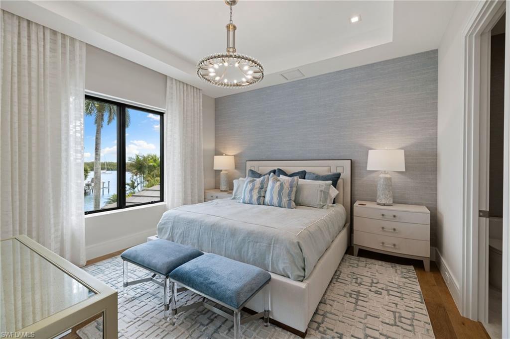 Bedroom featuring wallpapered walls, an accent wall, hanging lights, light wood-type flooring, and a water view