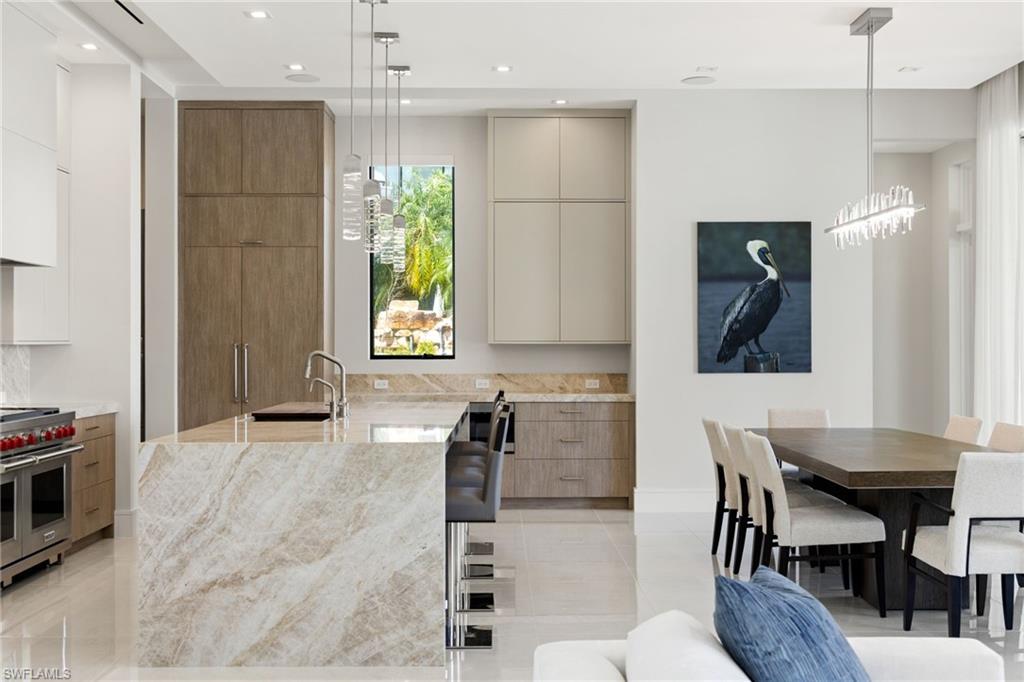 Dual tone kitchen with two tone color scheme, modern cabinets, light stone countertops, range with two ovens, and hanging light fixtures