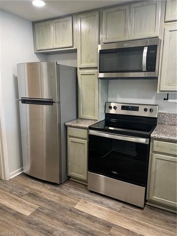 Kitchen featuring stainless steel appliances, dark wood-type flooring, and light stone counters