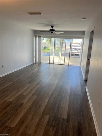 Empty room with a ceiling fan, healthy amount of natural light, dark wood-style flooring, and a water view