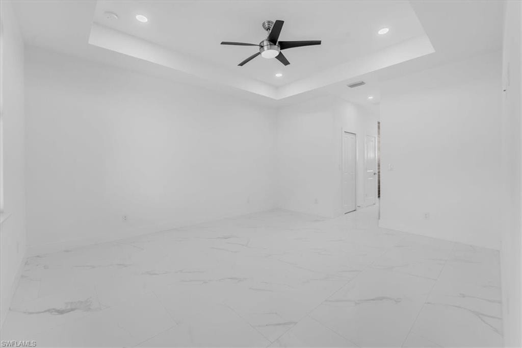 Unfurnished room featuring ceiling fan, light marble finish flooring, recessed lighting, and a raised ceiling