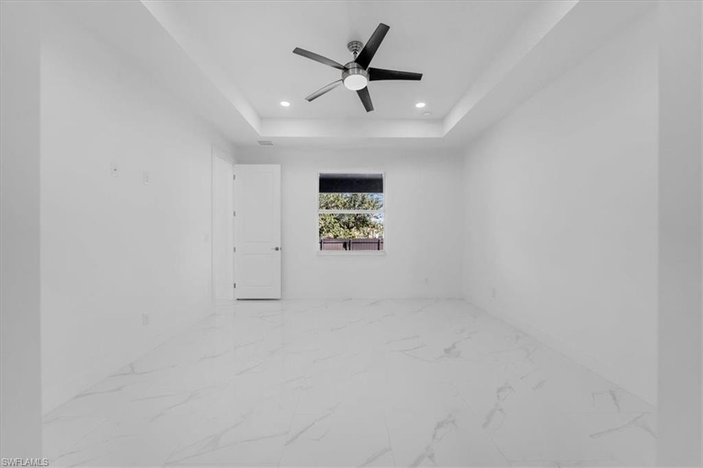 Spare room featuring light marble finish floors, a ceiling fan, recessed lighting, and a tray ceiling