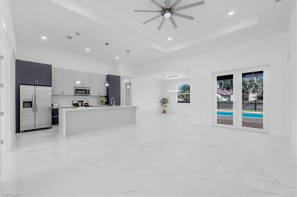 Kitchen featuring stainless steel appliances, open floor plan, a high tray ceiling, pendant lighting, and modern cabinets