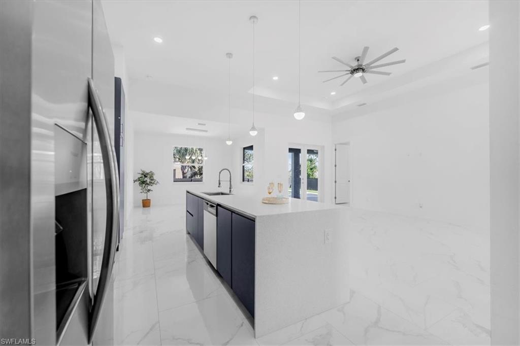 Kitchen featuring modern cabinets, stainless steel appliances, an island with sink, pendant lighting, and light stone counters