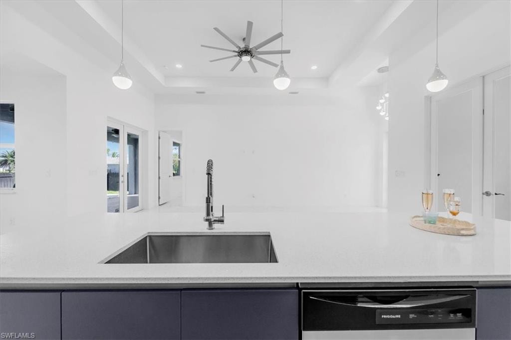 Kitchen featuring dishwasher, light stone countertops, a raised ceiling, and pendant lighting