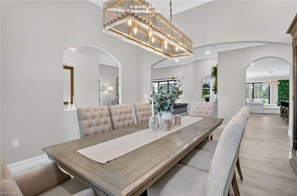 Dining area with ornamental molding, arched walkways, a high ceiling, light wood finished floors, and recessed lighting