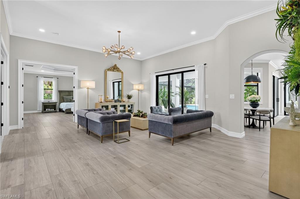 Living area featuring arched walkways, light wood-type flooring, hanging lights, and ornamental molding