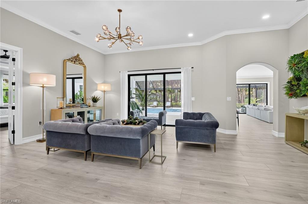 Living room with ornamental molding, arched walkways, light wood-style flooring, and suspended lighting