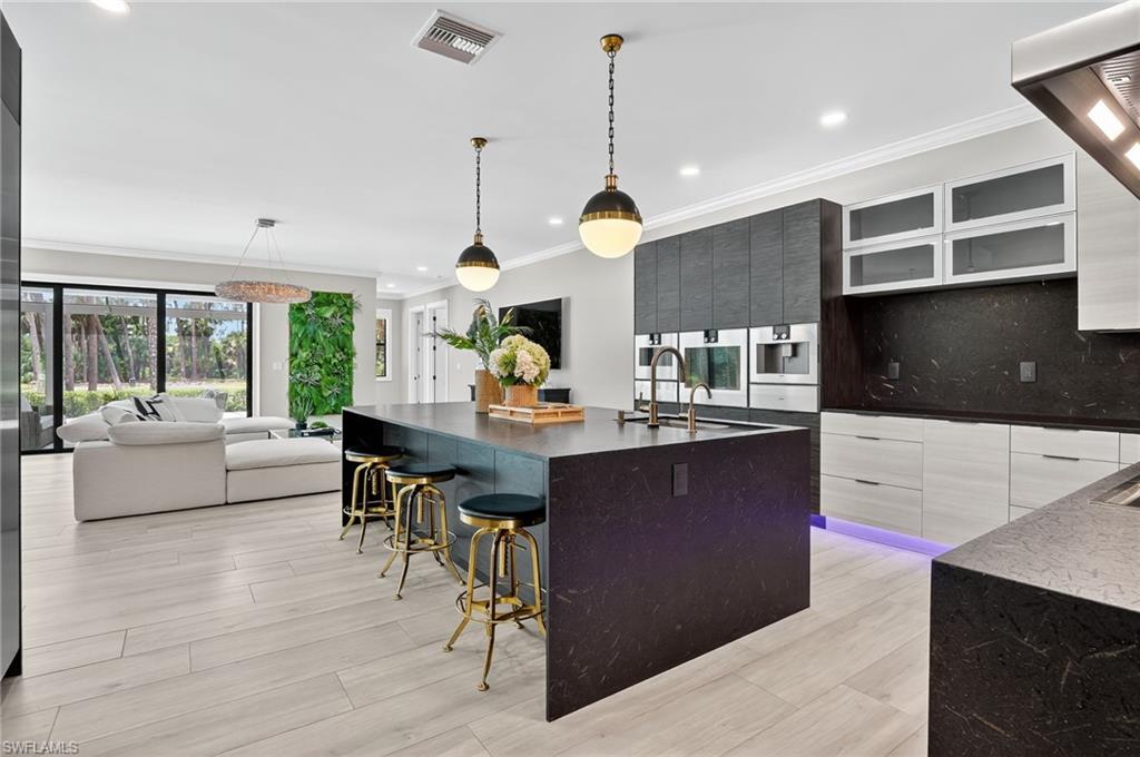 Kitchen with dark stone counters, a large island with sink, ventilation hood, open floor plan, and ornamental molding