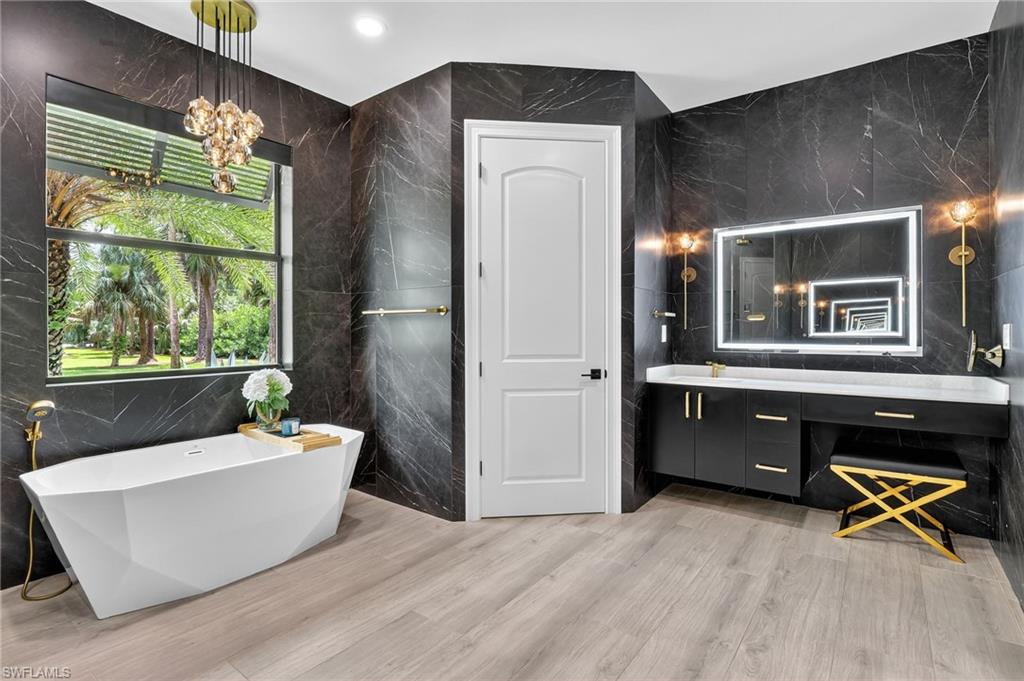 Full bathroom featuring tile walls, vanity, a soaking tub, a chandelier, and light wood finished floors