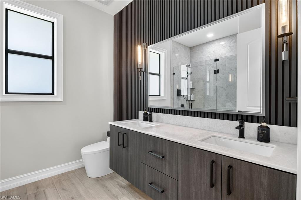 Bathroom featuring a shower stall, double vanity, and light wood finished floors