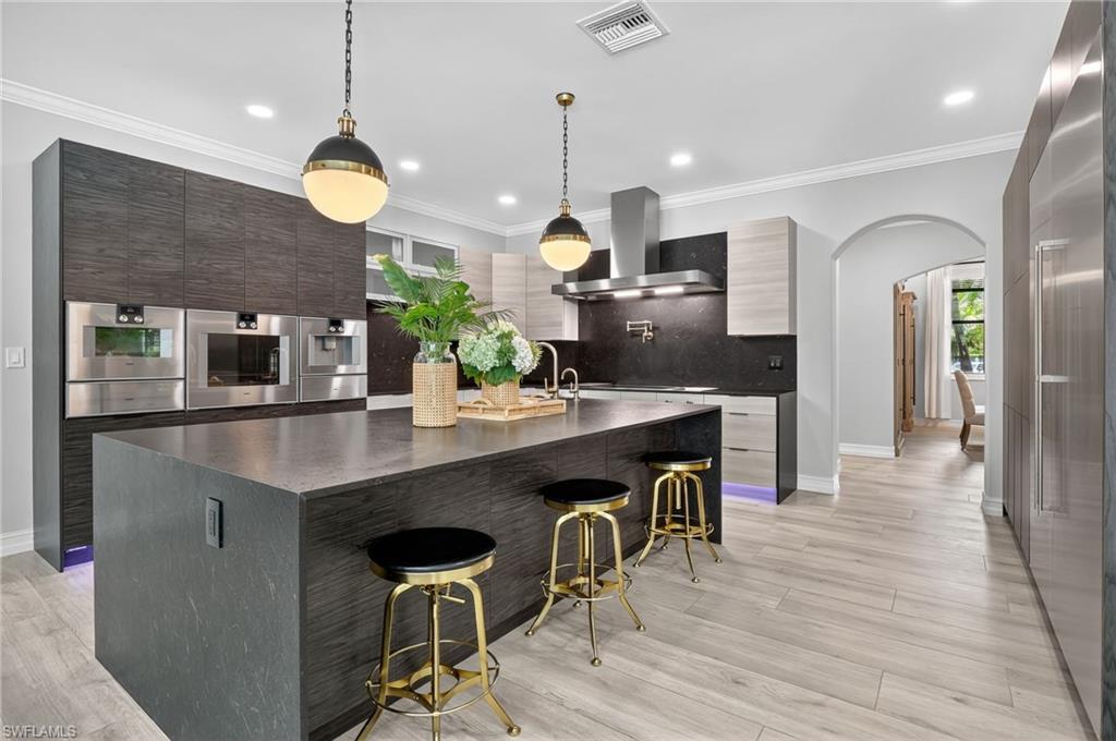 Kitchen featuring arched walkways, a breakfast bar, exhaust hood, dark stone counters, and pendant lighting