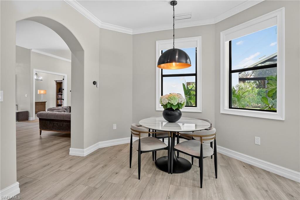 Dining area with crown molding, arched walkways, and light wood-type flooring