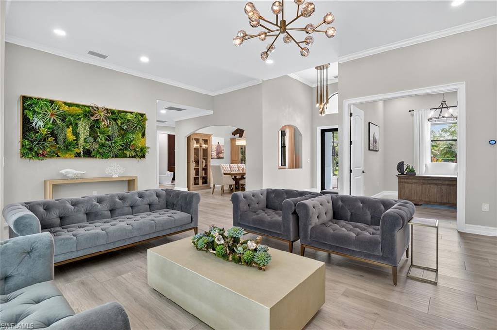 Living room with light wood-type flooring, arched walkways, suspended lighting, and crown molding