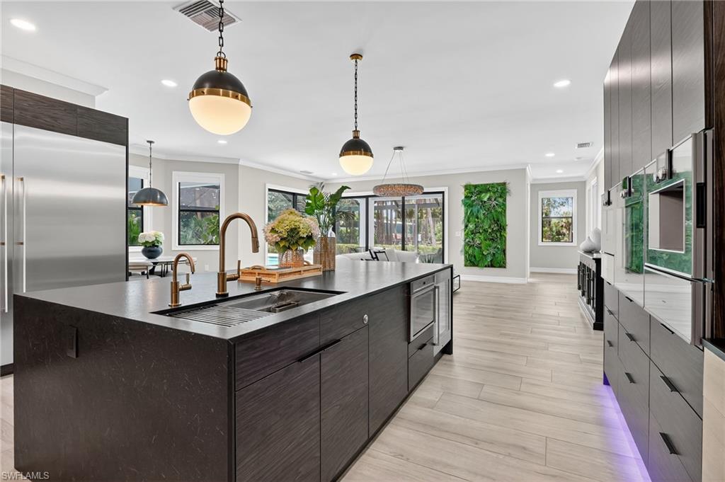 Kitchen with dark wood finish cabinets, modern cabinets, an island with sink, stainless steel appliances, and crown molding