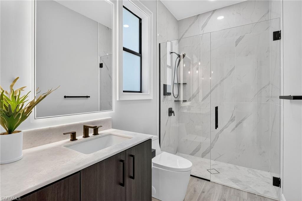 Full bath featuring a marble finish shower, vanity, and light wood finished floors