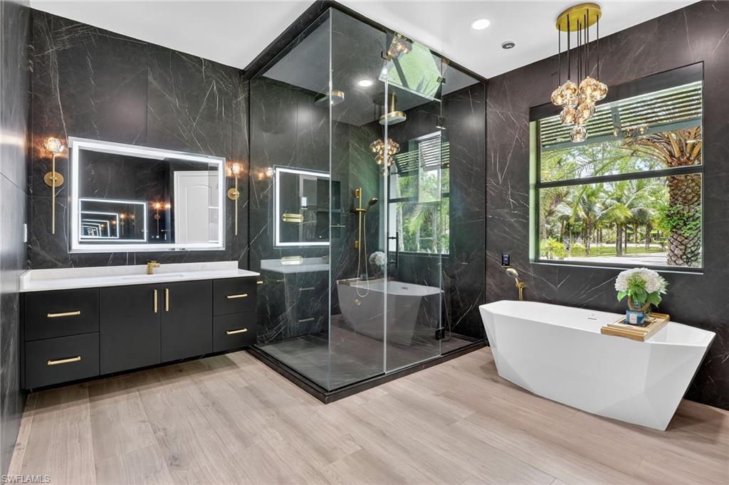 Bathroom with tile walls, vanity, a freestanding bath, a marble finish shower, and stone wall