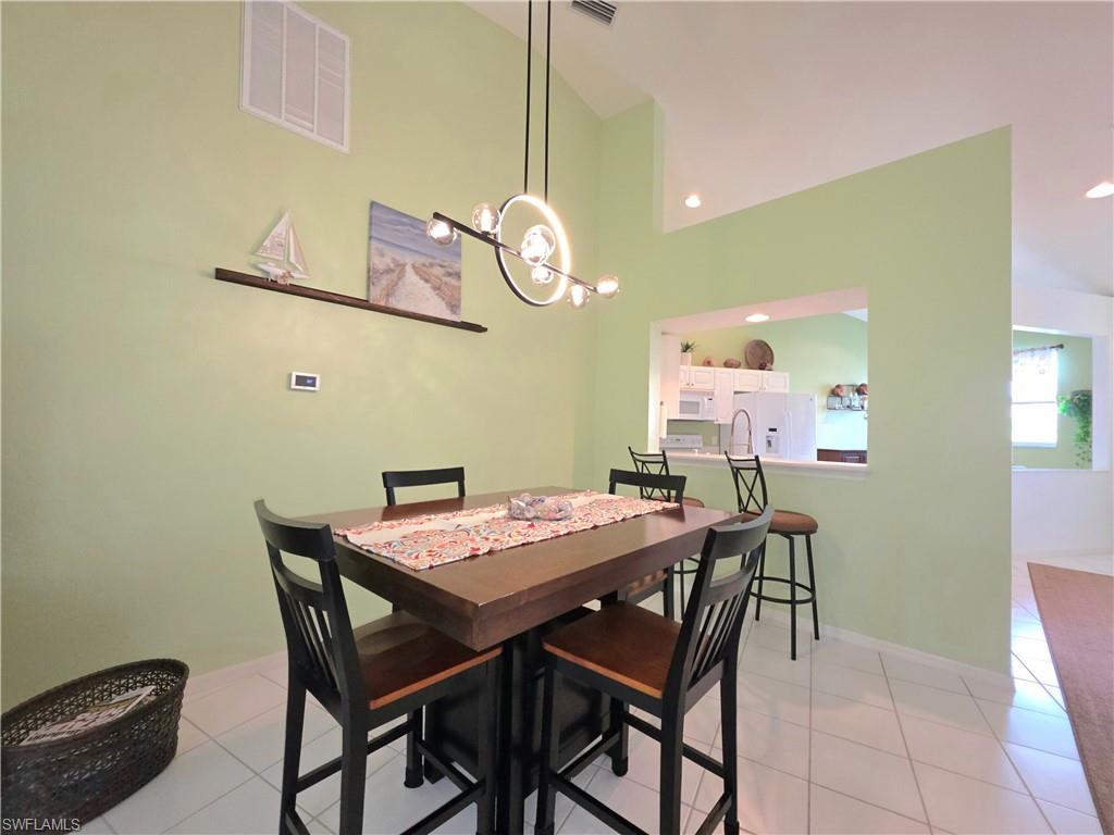 Dining space with light tile patterned floors, a chandelier, and vaulted ceiling