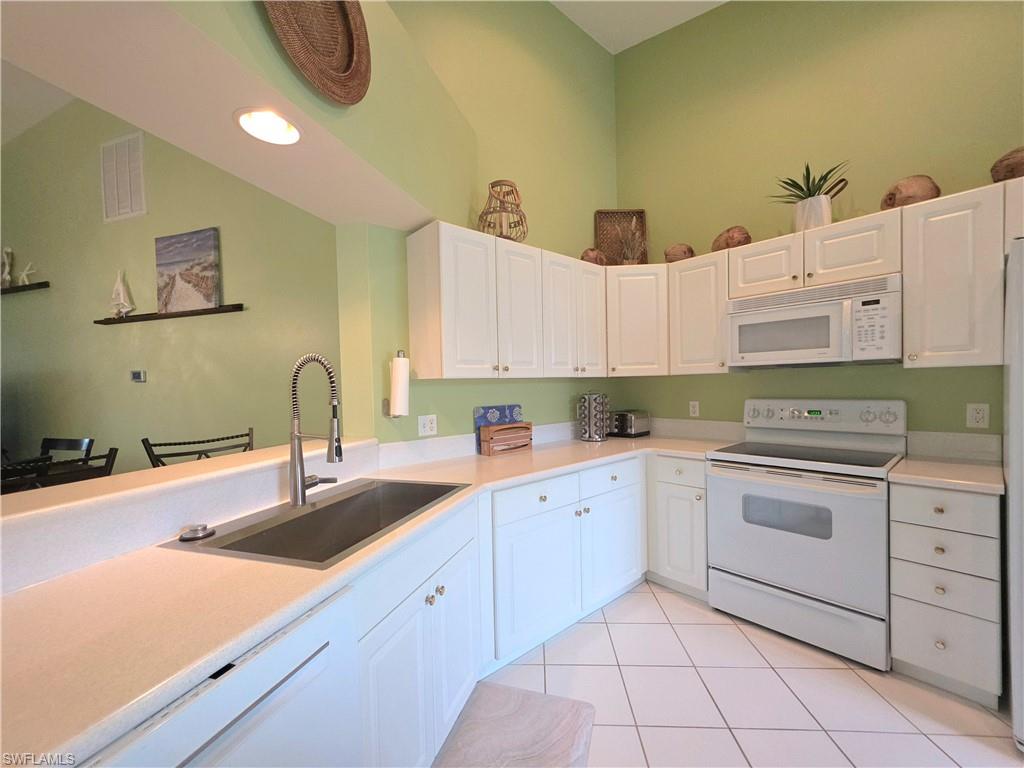 Kitchen featuring white appliances, white cabinets, light countertops, light tile patterned floors, and a high ceiling