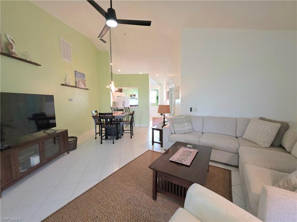 Living room with light tile patterned flooring, ceiling fan, and lofted ceiling