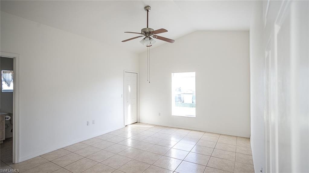 Unfurnished room with lofted ceiling, ceiling fan, and light tile patterned floors