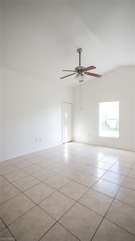 Empty room with ceiling fan, vaulted ceiling, and light tile patterned floors