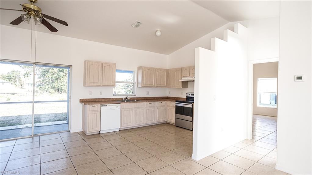 Kitchen featuring stainless steel range with electric stovetop, white dishwasher, ceiling fan, light tile patterned floors, and vaulted ceiling