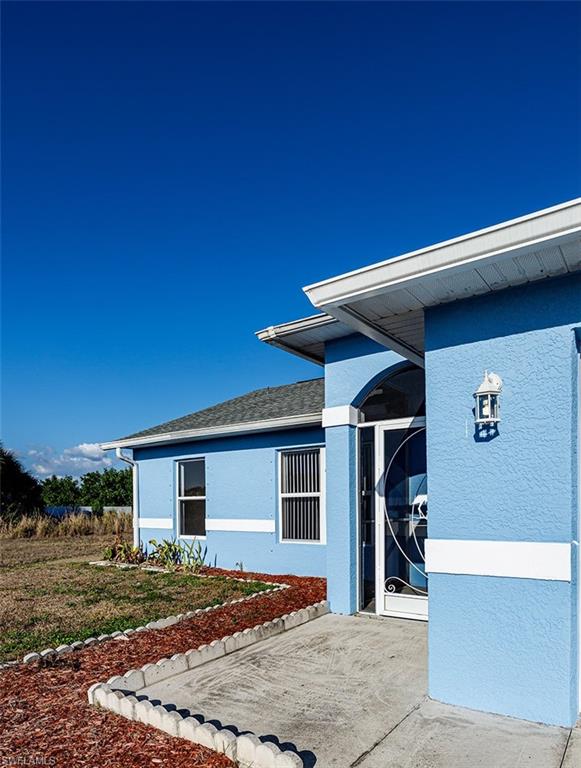 Property entrance featuring stucco siding and roof with shingles
