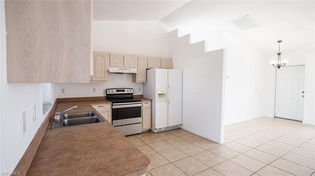 Kitchen with stainless steel electric range, white refrigerator with ice dispenser, a chandelier, light wood finish cabinets, and vaulted ceiling