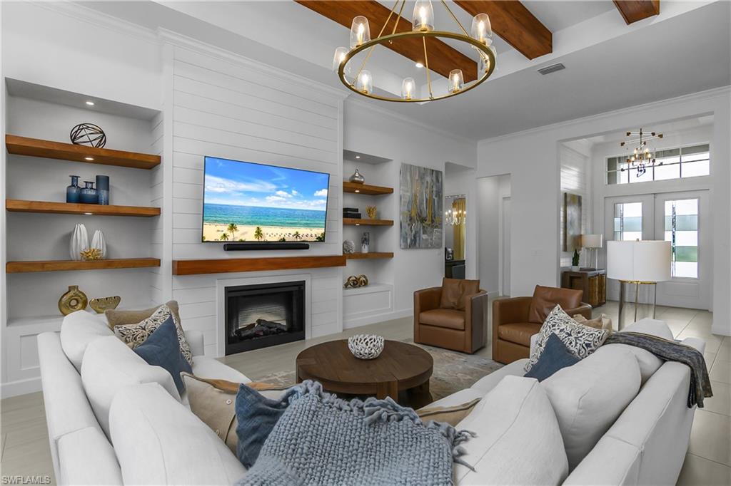 Living area featuring hanging lights, built in shelves, a fireplace, ornamental molding, and beamed ceiling