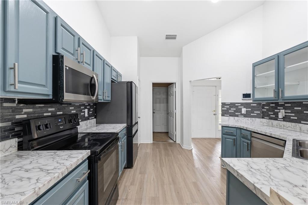 Kitchen featuring blue cabinets, black appliances, tasteful backsplash, light countertops, and glass insert cabinets