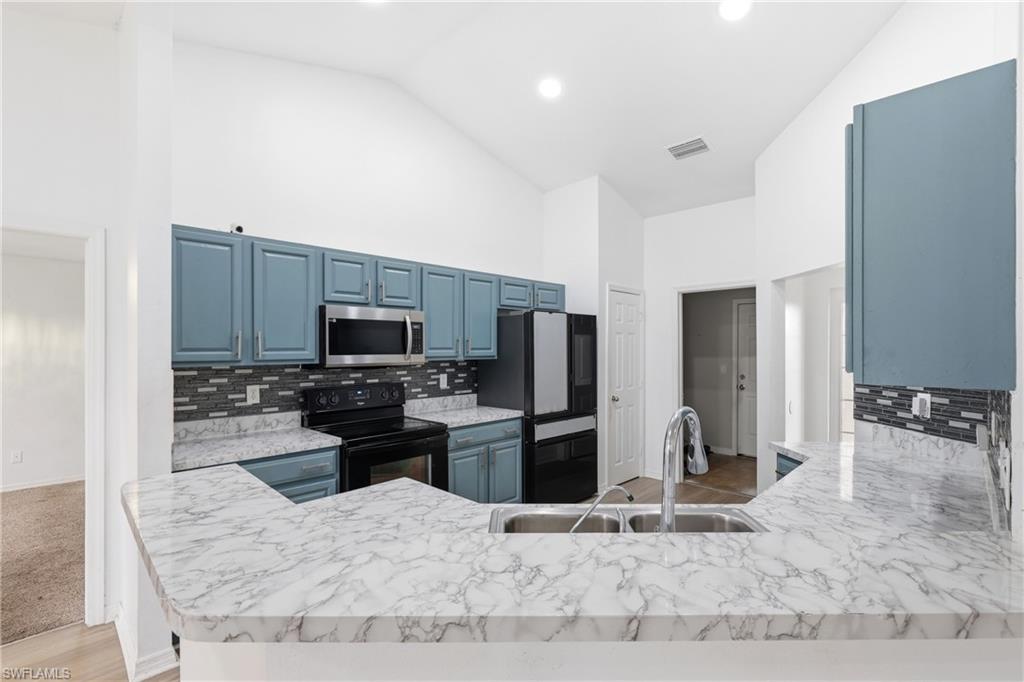 Kitchen with black appliances, vaulted ceiling, blue cabinets, tasteful backsplash, and a peninsula