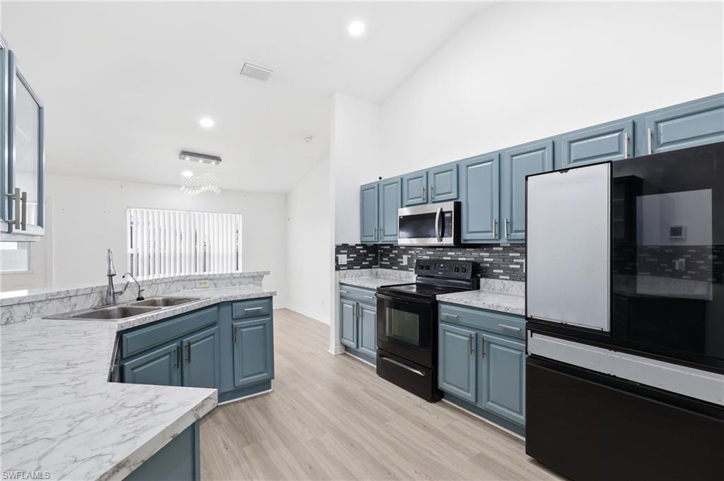 Kitchen with smart refrigerator, blue cabinets, light countertops, vaulted ceiling, and black range with electric stovetop
