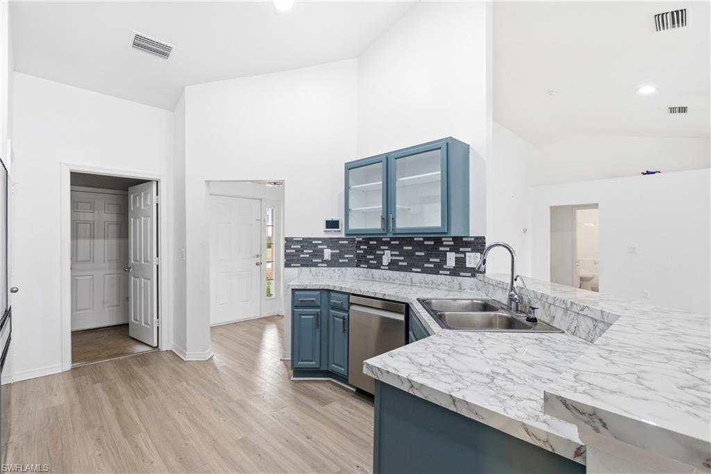 Kitchen with blue cabinetry, a peninsula, glass insert cabinets, lofted ceiling, and light wood finished floors