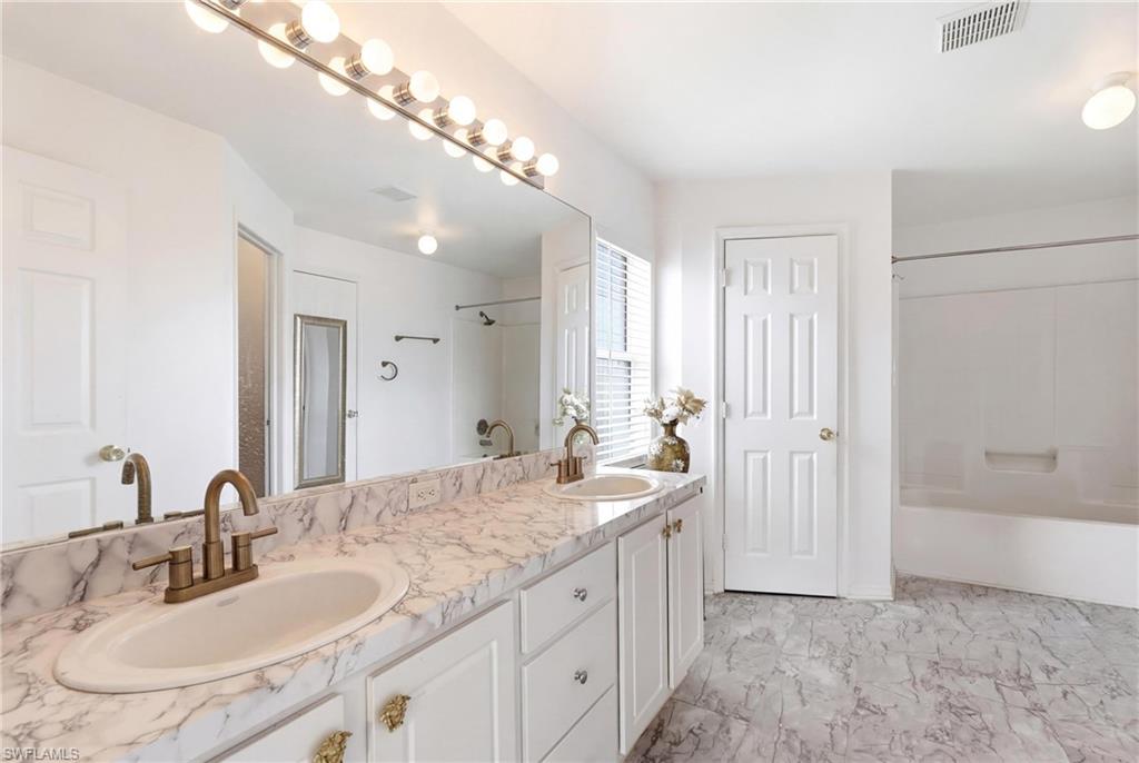 Bathroom with double vanity, light marble finish flooring, and shower / washtub combination