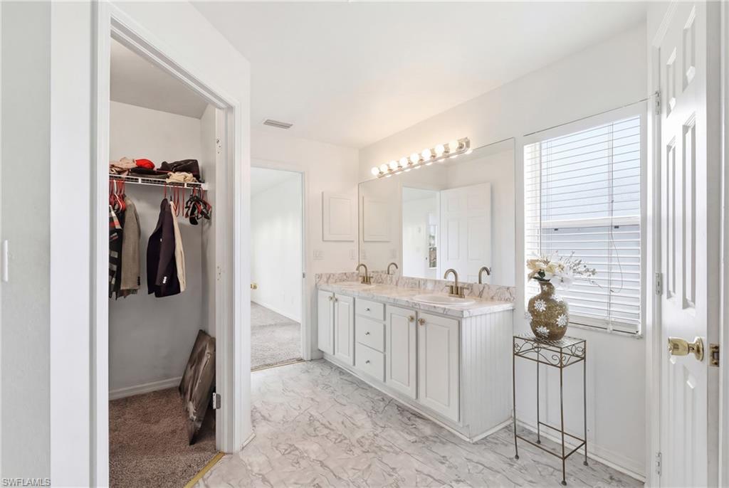 Bathroom with double vanity, light marble finish flooring, and a spacious closet