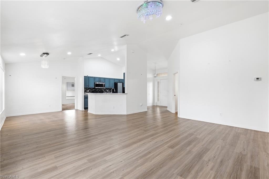 Unfurnished living room featuring hanging lights, lofted ceiling, and light wood finished floors