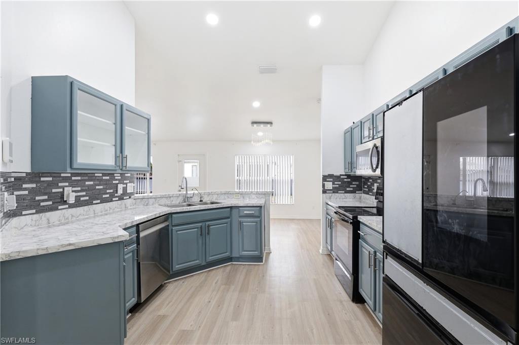 Kitchen with stainless steel appliances, a peninsula, blue cabinets, glass fronted cabinets, and light wood finished floors