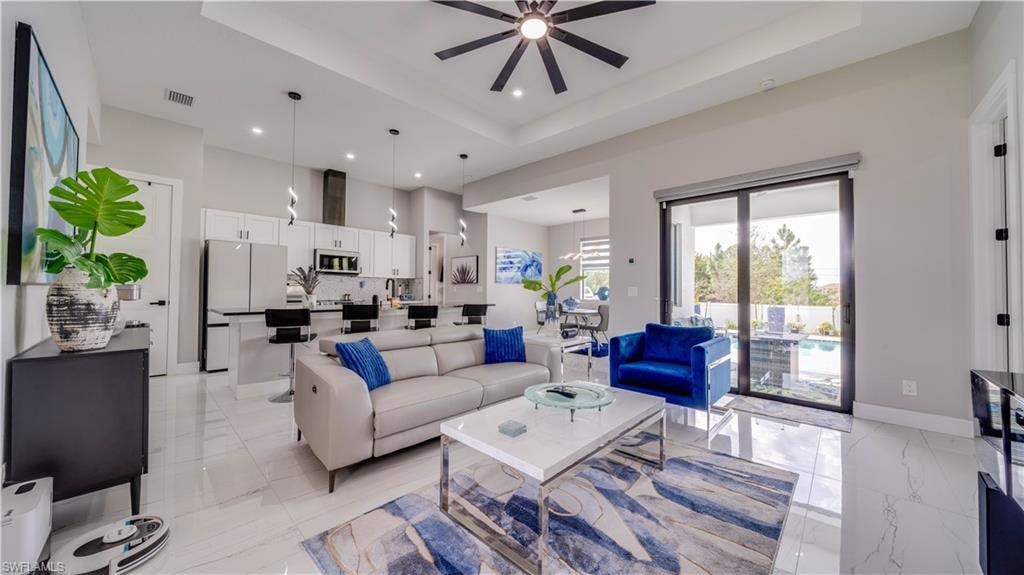 Open concept Great room. Living area featuring ceiling fan, high tray ceiling, and sliders to pool area