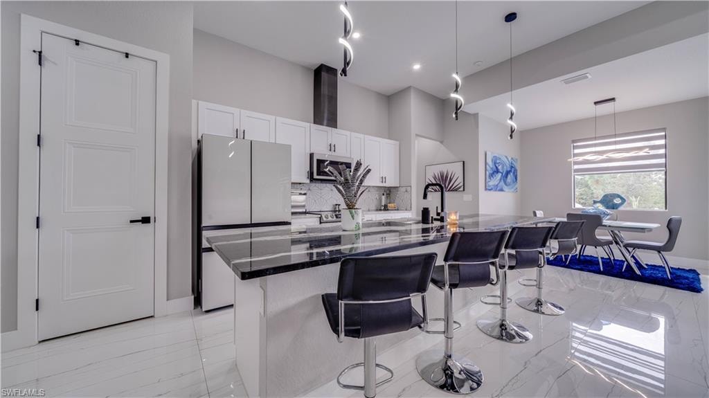 Kitchen featuring island with sink, beautiful granite counters, white cabinetry, and a pantry