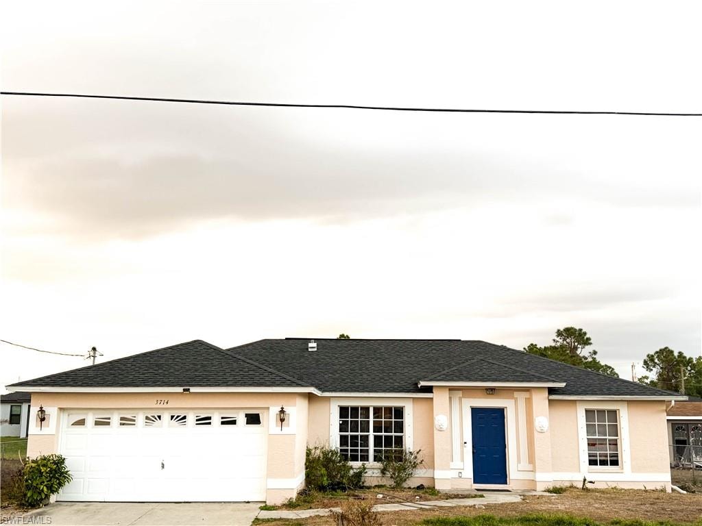 Single story home with driveway, stucco siding, a garage, and roof with shingles