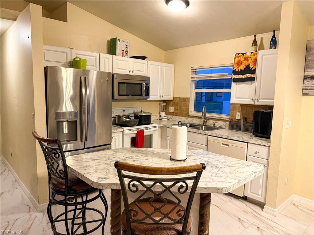 Kitchen featuring light countertops, light marble finish flooring, stainless steel appliances, white cabinets, and lofted ceiling