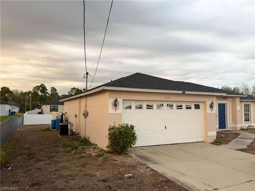 View of side of property featuring a garage, stucco siding, concrete driveway, and roof with shingles