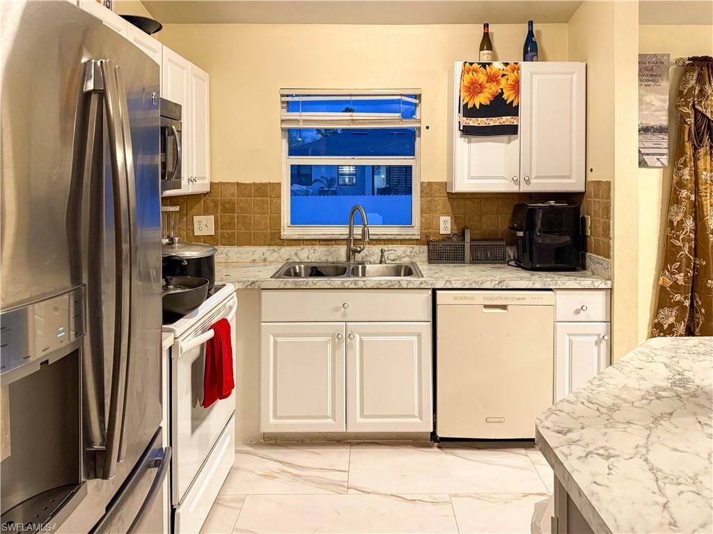Kitchen featuring stainless steel appliances, light countertops, white cabinetry, light marble finish floors, and backsplash