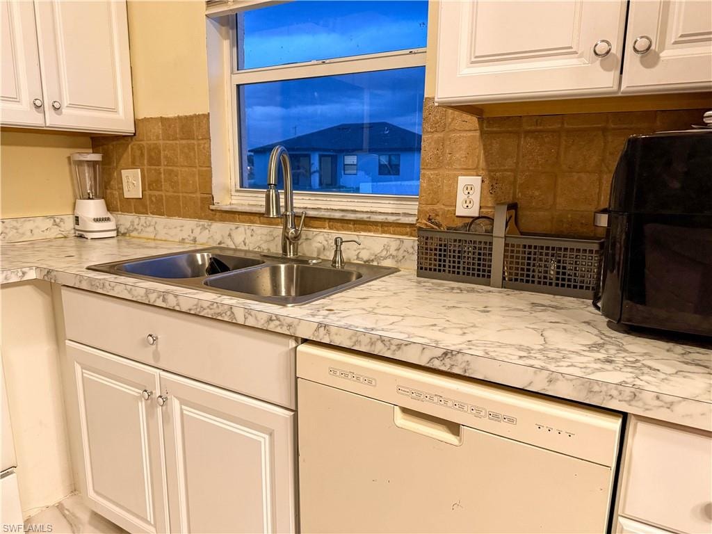 Kitchen with white dishwasher, white cabinets, backsplash, light countertops, and black microwave