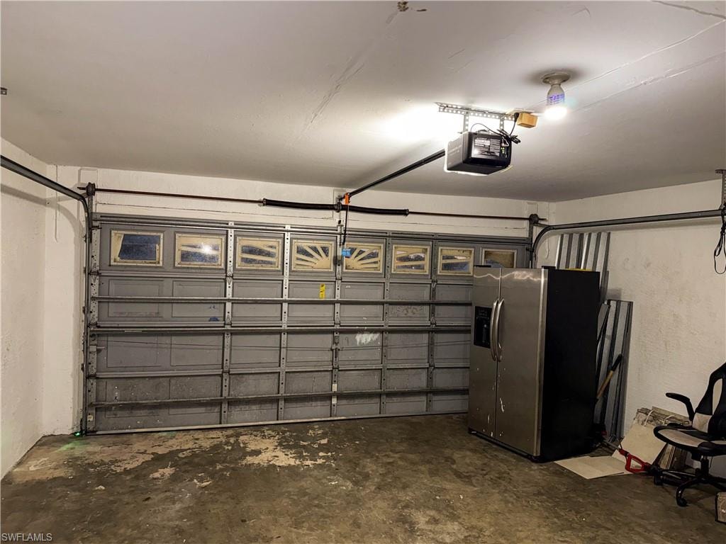 Garage featuring stainless steel fridge and a garage door opener