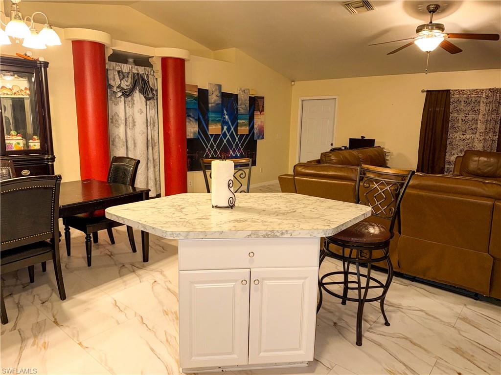 Kitchen featuring light marble finish floors, open floor plan, light countertops, a kitchen bar, and a center island